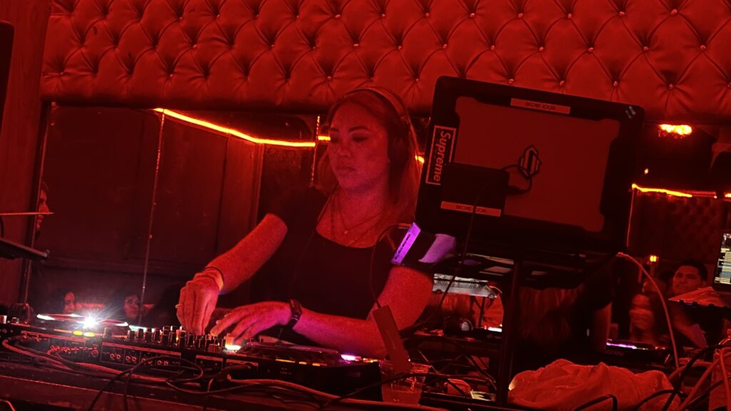 DJ Beckie Joon performing in a dimly lit venue with red lighting, focused on the turntable.