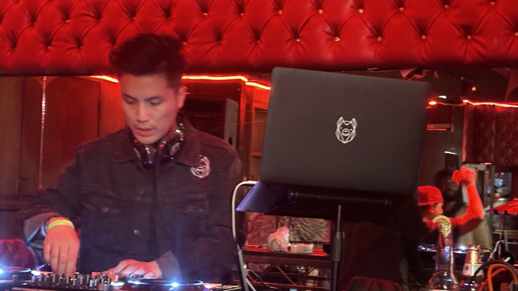 DJ Ghostbear performing in a vibrant venue with red lighting, focused on mixing music.